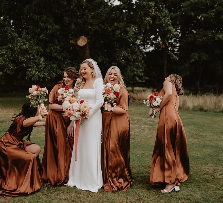 Bride in corset look bodice satin wedding dress and bridal party wearing burnt orange satin bridesmaid dresses with matching mixed colourful floral bouquets