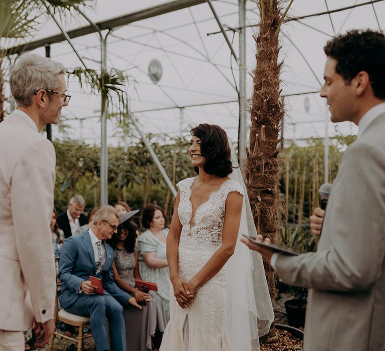 Bride & Groom smile lovingly at each other during ceremony at greenhouse style venue