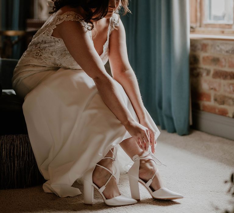 Bride wears strappy bridal heels and lace wedding dress on as she prepares on the morning of her wedding day