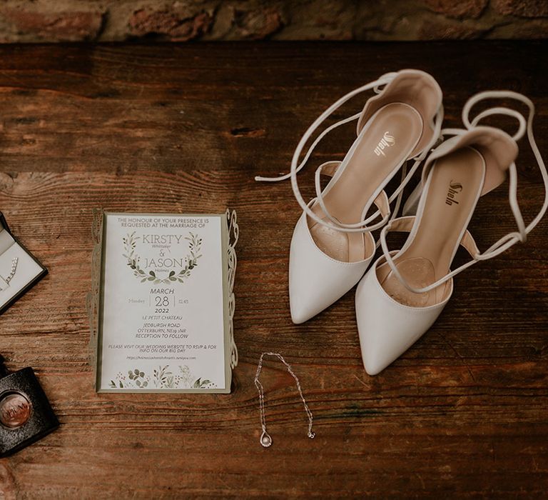 Wedding stationery beside white strappy bridal heels and wedding jewellery 