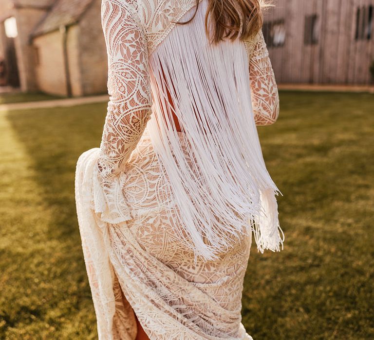 Close up of bride's long-sleeve boho wedding dress with open back detailing and long white tassels 