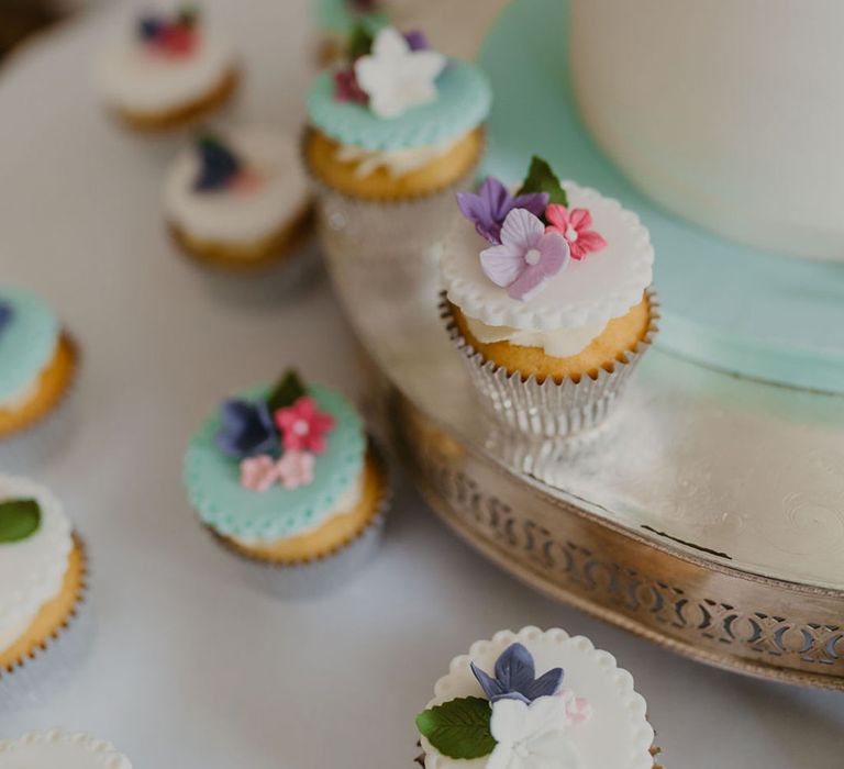 Mini pastel cupcakes surrounded wedding cake finished with floral fondant decor 