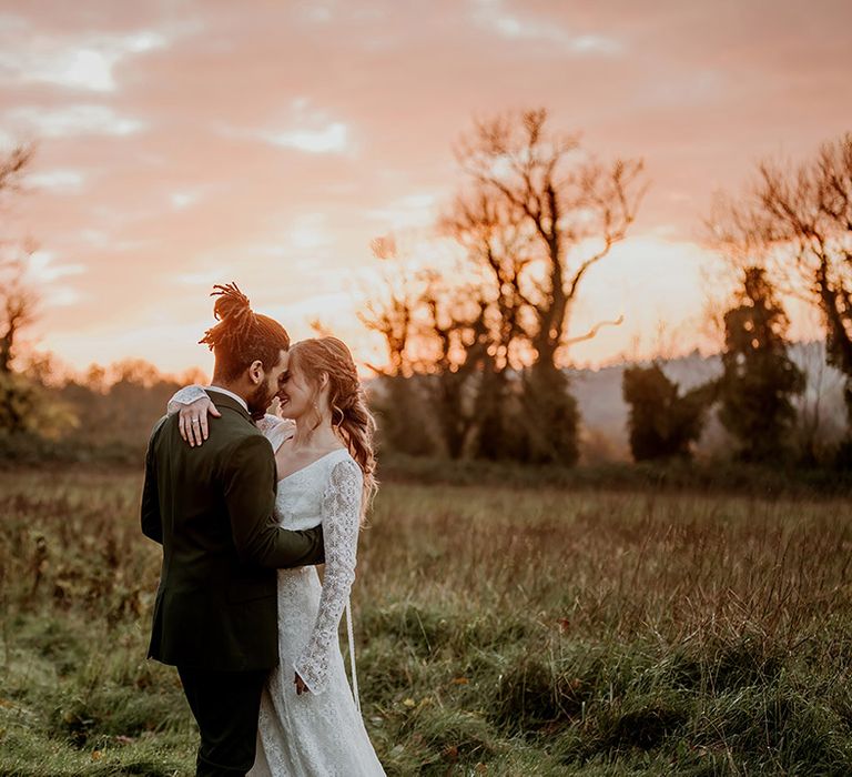 Groom in classic black tux and bride in long sleeve boho lace wedding dress doing couples golden hour shoot at barn wedding venue 