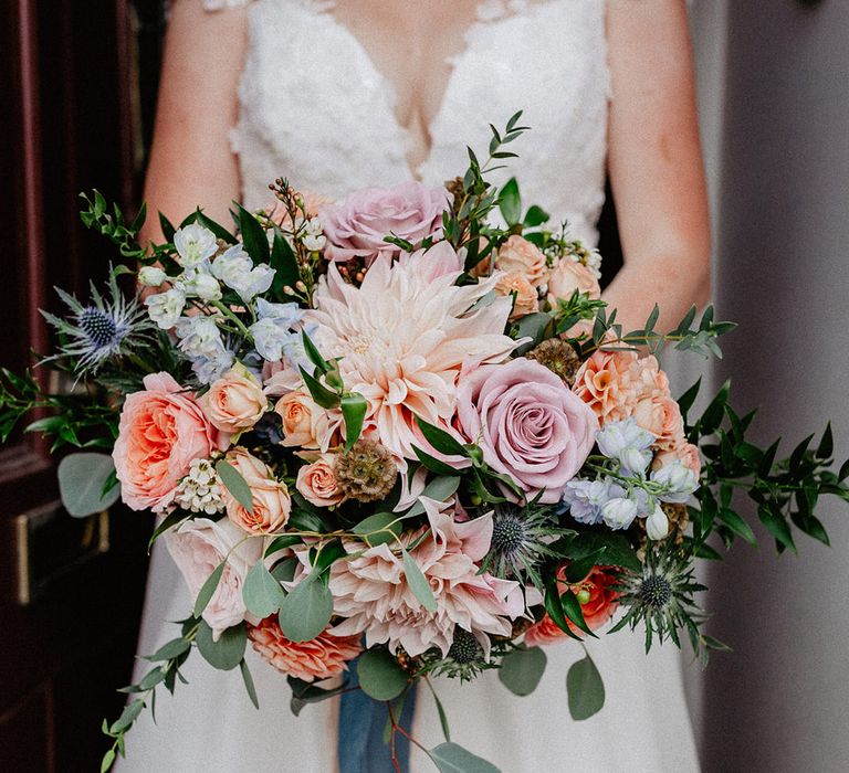 Pink, purple, blue, and peach spring wedding bouquet for the bride with roses and thistle tied with blue ribbon 