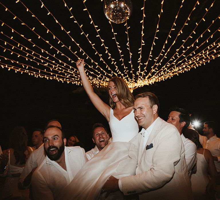 Bride is lifted by guests during wedding reception complete with fairy light canopy hanging above