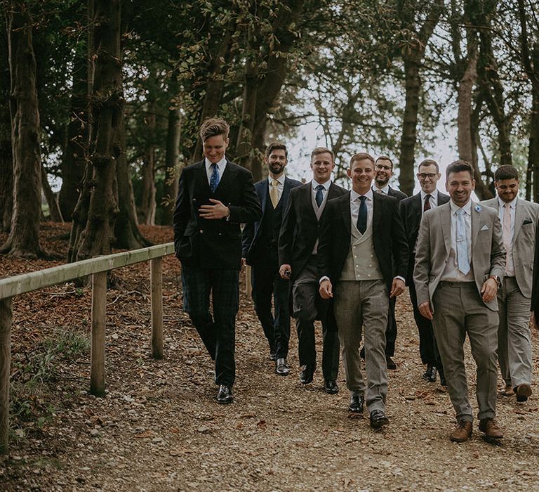 Groom walks alongside his groomsmen in mismatched styled Morning Suits and different coloured ties 