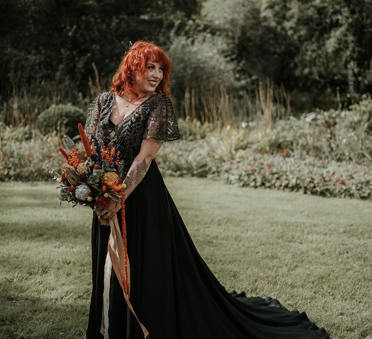 Bride in embellished short sleeve v-neck black wedding dress with large burnt orange and eucalyptus dried flower bouquet 