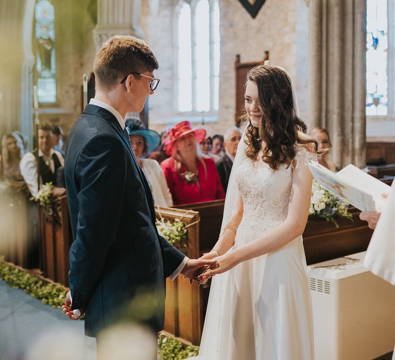 Groom in navy wedding suit with glasses facing the bride for the wedding day at their religious church wedding 