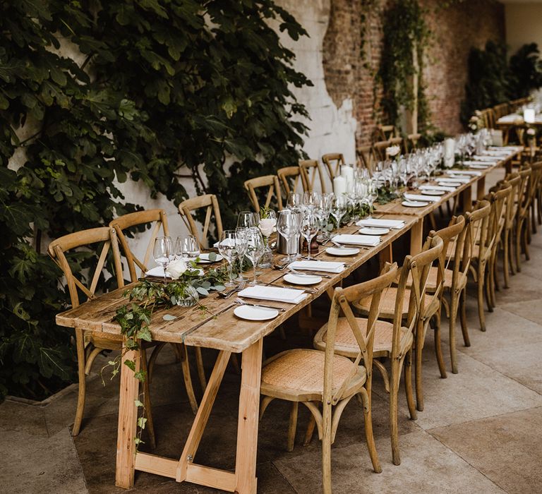 The simple wedding tablescape with foliage table runners, white plating, silver cutlery, and bud vases with pink roses and gypsophila 