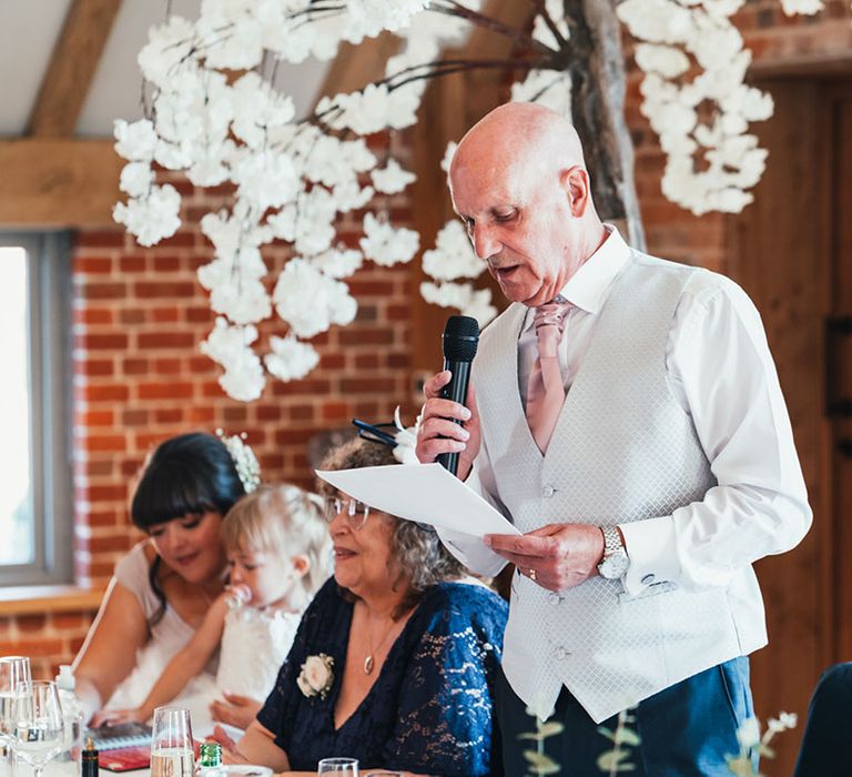 Father of the bride in a light grey waistcoat and pink tie reading out his speech at the reception 