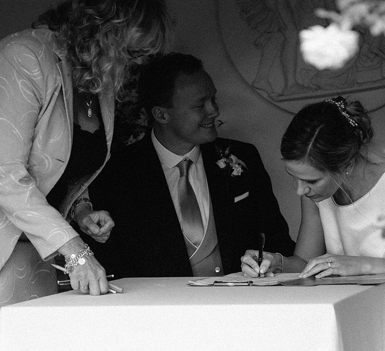 Bride in high neck wedding dress signing the wedding register with the groom for their hotel wedding venue 