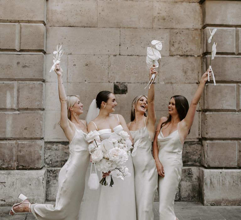 Bridesmaids in white satin bridesmaid dresses with the bride in a sleek wedding dress with their white wedding bouquets 