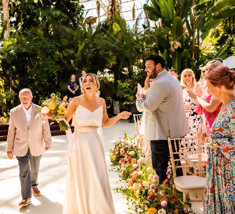 Bride in satin bridal separates two piece from Catherine Deane walking down the aisle with the father of the bride 