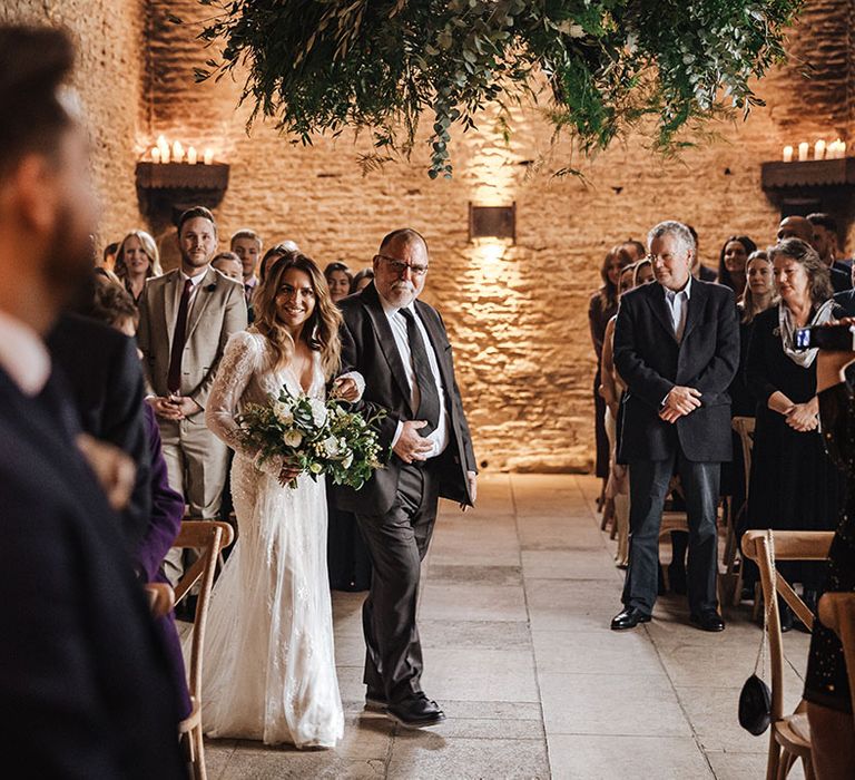 Rustic barn wedding with the bride being walked down the aisle by her father to meet the groom at the end 