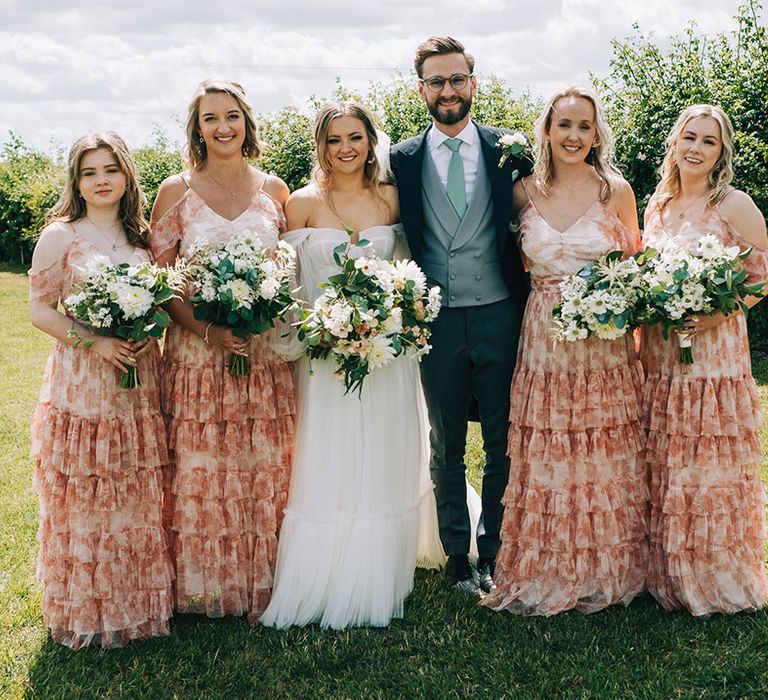 Bridesmaids in matching patterned bridesmaid dresses for the summer festival wedding posing with the bride and groom 