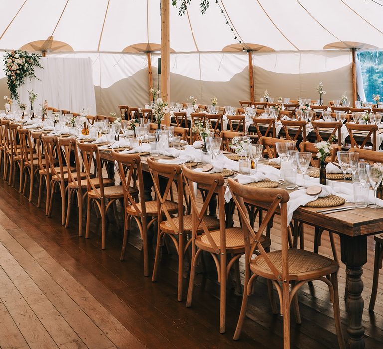 Simple and neutral wedding table decor with white flowers, wicker place mats, wood slice place names in the marquee 