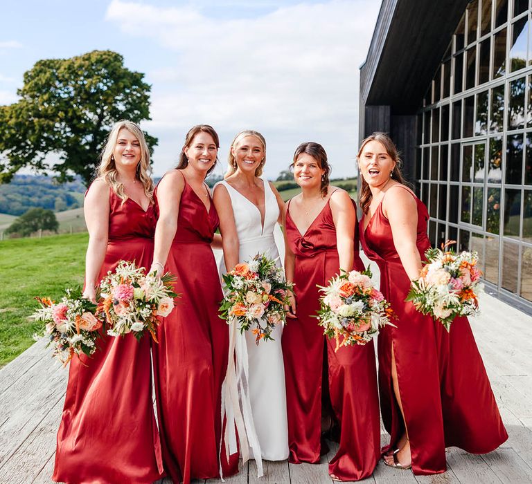 Bridesmaids in red copper satin bridesmaid dresses with the bride in her fitted white wedding dress 