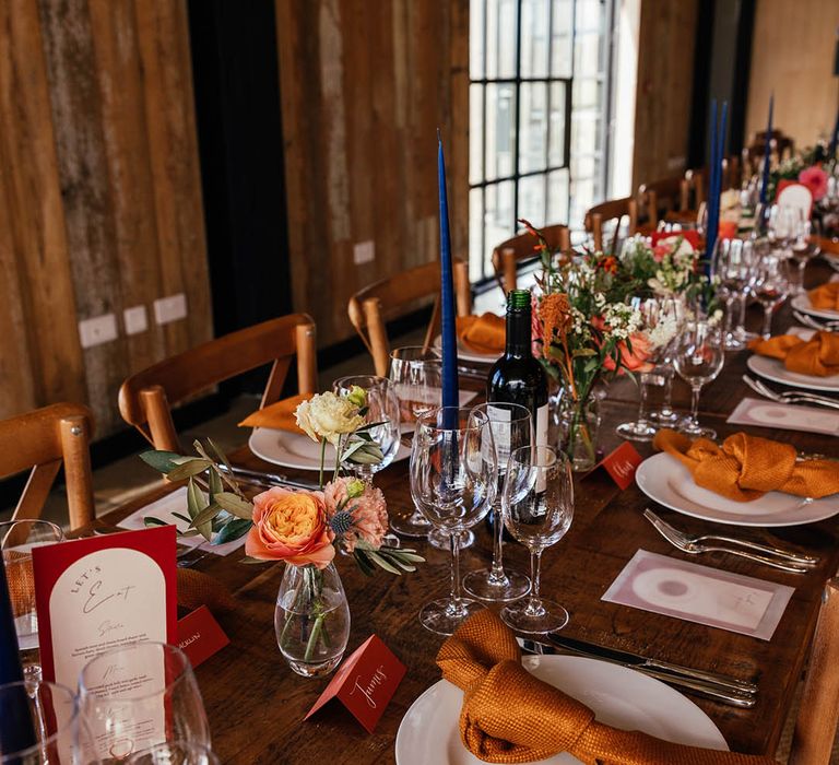 Tall blue taper candle with orange and copper theme wedding place setting for autumnal barn wedding 