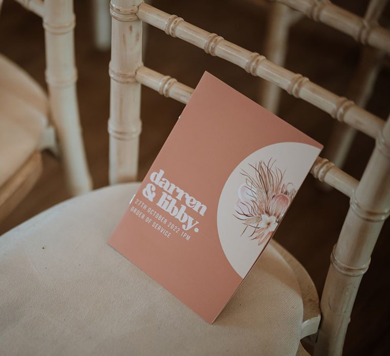 Matching terracotta peach and white wedding order of service cards resting on each guest's chair 