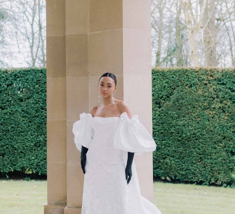 Bride in strapless lace wedding dress with detachable puff sleeves, train and black satin gloves at Settrington Orangery editorial shoot