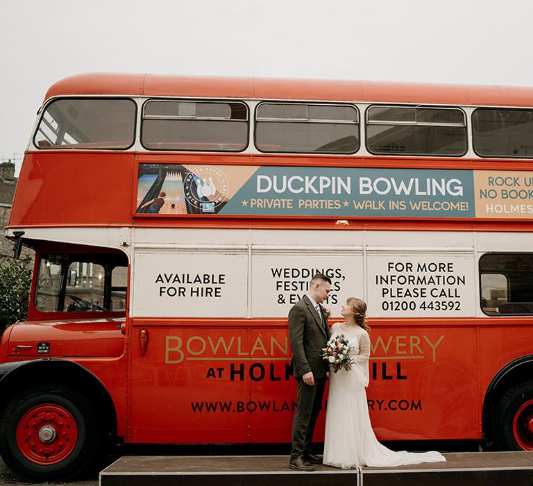 The bride and groom pose in front of the red double decker bus wedding transport 