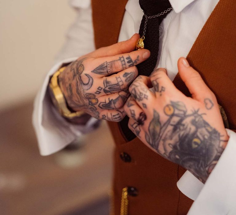 Bride wearing gold watch tying up black tie onto her bridal suit at Kingscote Barn Tetbury 