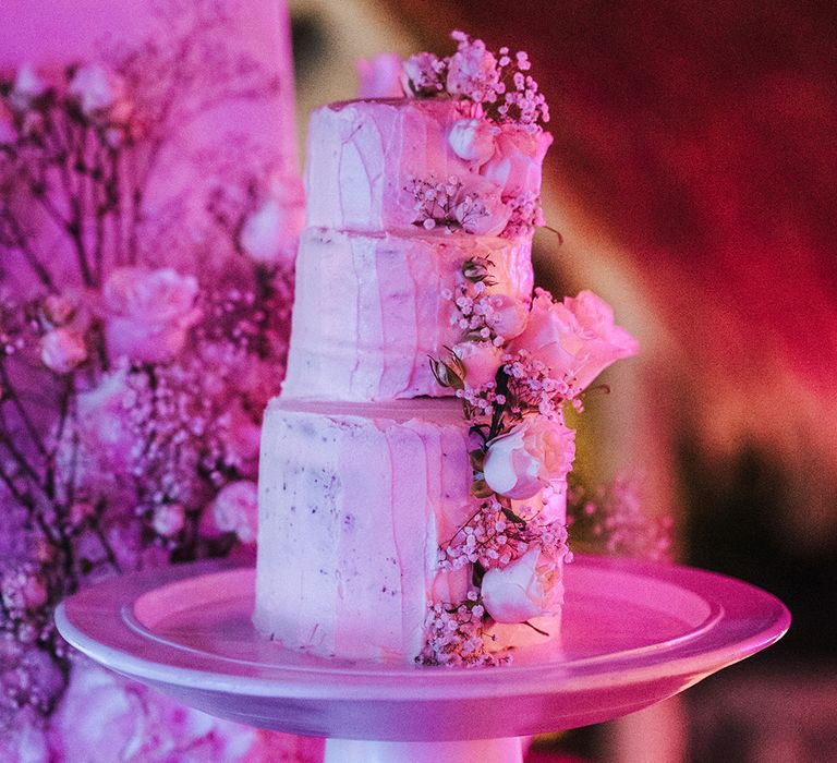 three tier wedding cake with roses and gypsophila decoration on a white cake stand