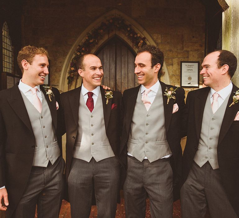 Groom and groomsmen in dark there piece suits with light grey waistcoat and pink ties with a red tie for the groom 