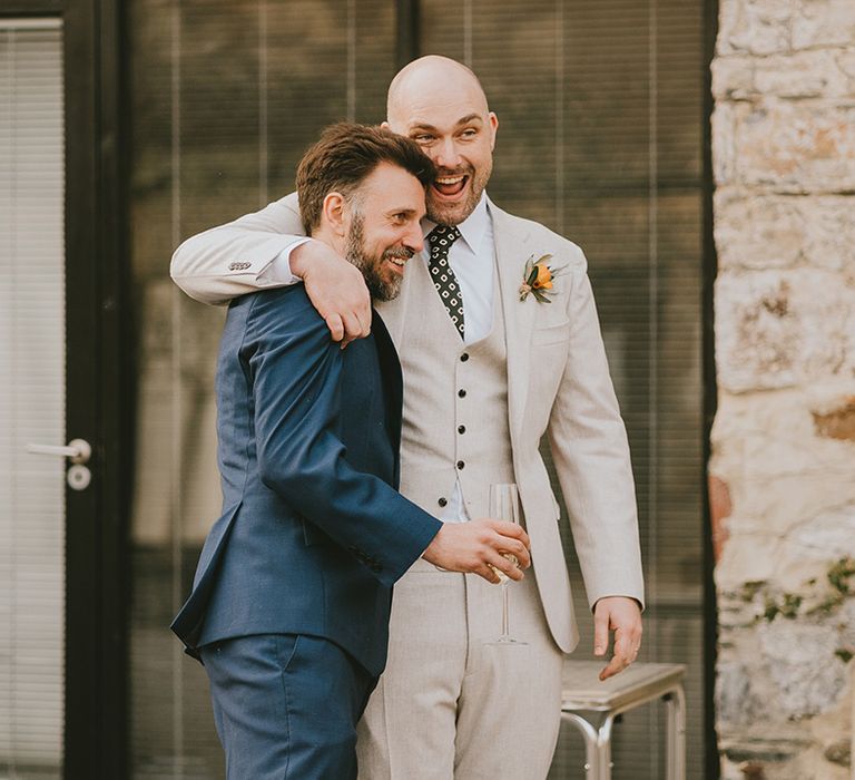 Groom in cream three piece wedding suit embracing a groomsman 