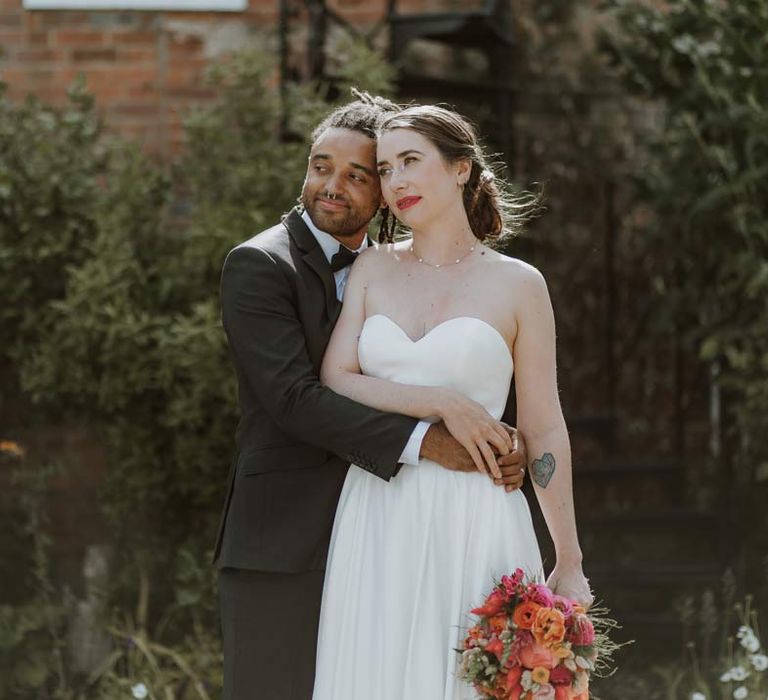 Bride in strapless sweetheart neckline wedding dress holding pink and orange wedding bouquet with groom in classic black tuxedo with bowtie and pink and orange wedding boutonniere 