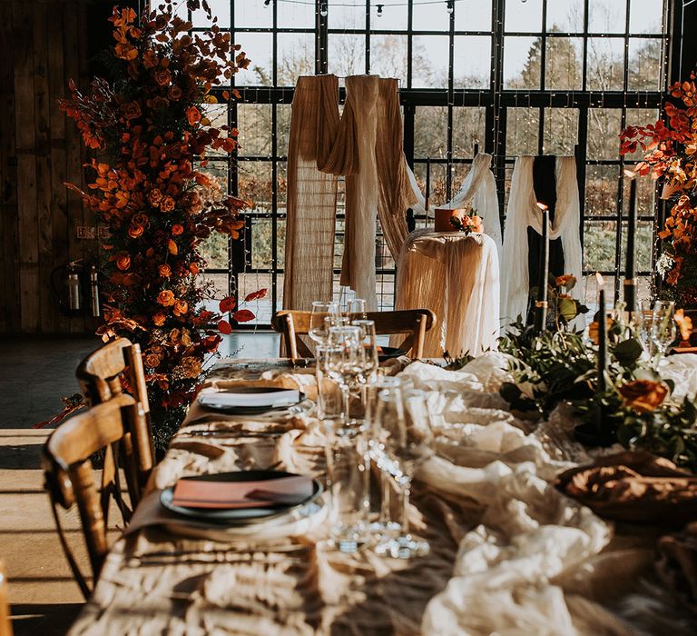 Orange autumn leaf flower columns with white drapery on the wedding tables with black taper candles 