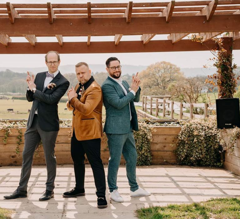 Groom in crushed velvet burnt orange grooms blazer and dried flower boutonniere standing and posing with groomsmen in mismatched groomsmen outfits at Southlands Barn