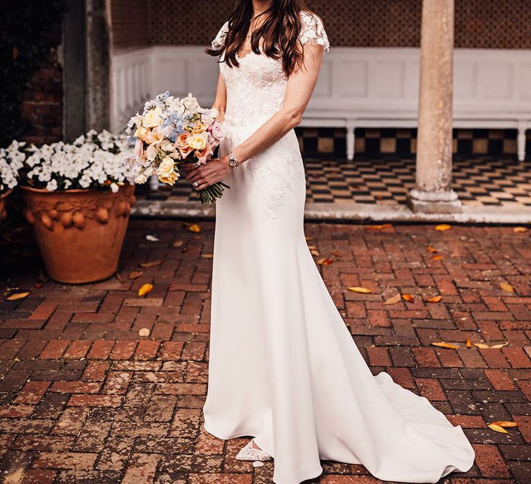 Bride in lace floral wedding dress holding pink, blue and yellow pastel wedding bouquet 