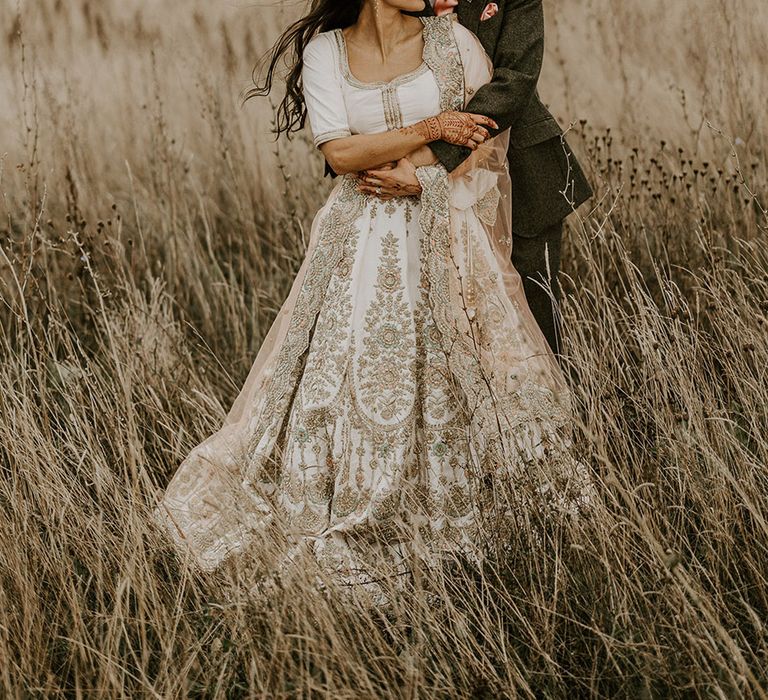 Groom wearing silk pink tie and pocket square embraces the bride from behind for cute couple photo 