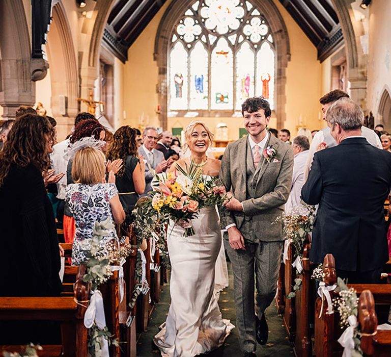 The bride and groom walk back down the aisle together after their church ceremony 