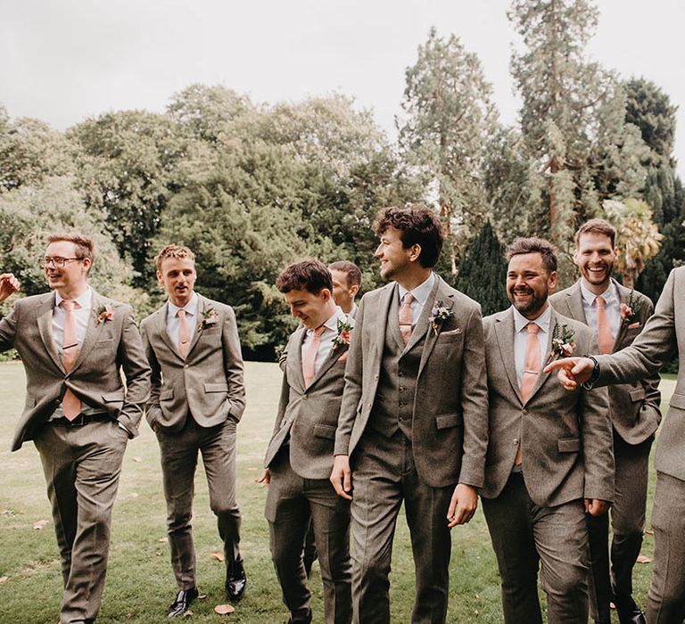 The groomsmen in grey tweed suits walk together with the groom 