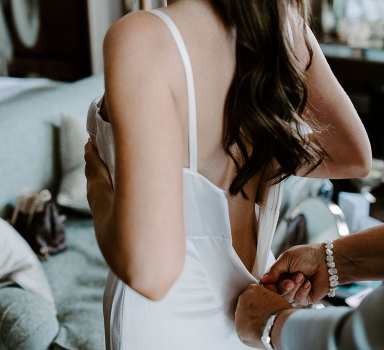 Bride getting into wedding dress wearing her hair in a slick ponytail 