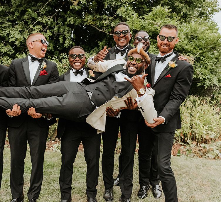 Groomsmen in black tuxedos holding up the groom of fun group wedding photo 