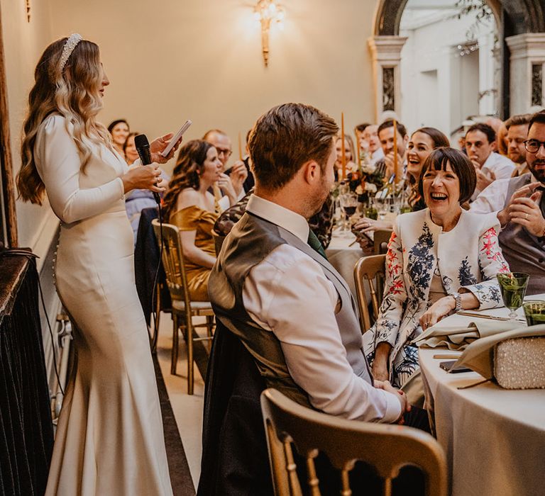 Bride stands up to read out her wedding speech as the guests laugh listening 