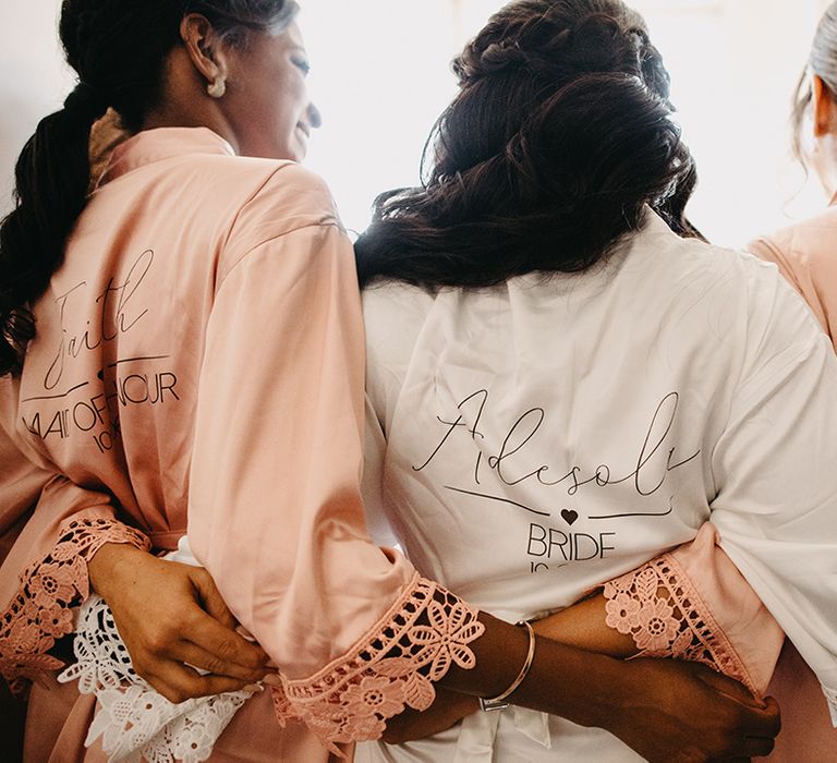 Bride in white custom robe standing with bridesmaids in light pink robes 