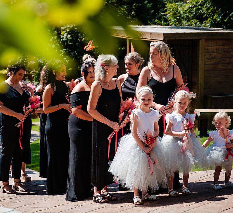 Bridal party wearing black bridesmaid dresses with two flower girls in white tutu dresses 