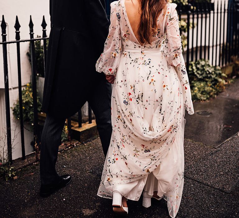 Bride wearing floral embroidered wedding dress with groom in three piece morning suit walking in London 