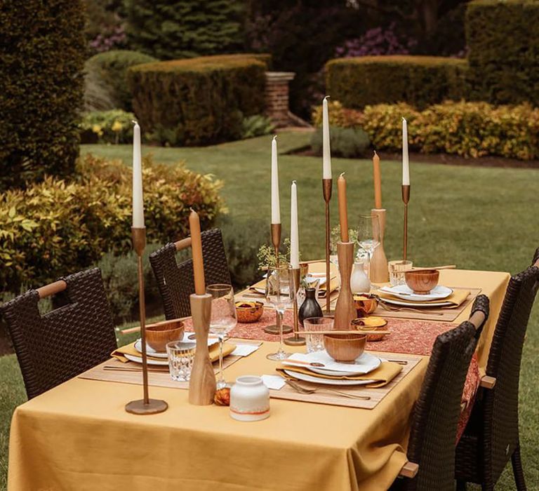 Yellow theme wedding tablescape with a yellow tablecloth with white and orange candles 