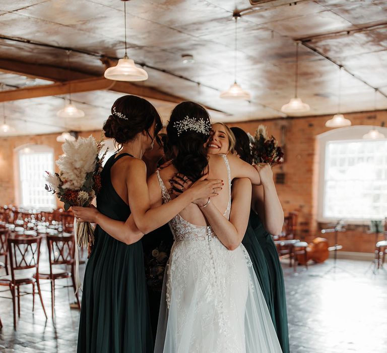 Bridal party in dark green bridesmaid dresses hugging the bride for cute group photo 