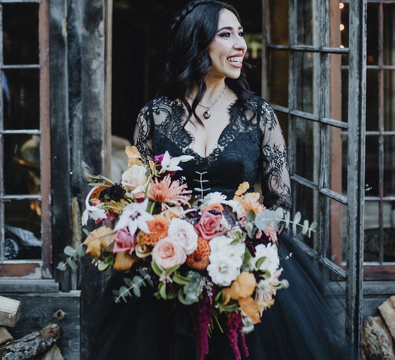 Bride in black lace wedding dress with autumnal bouquet with pink and yellow blooms 