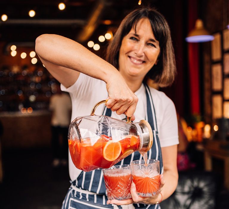 Waiter serving wedding cocktail from glass jug to guests 