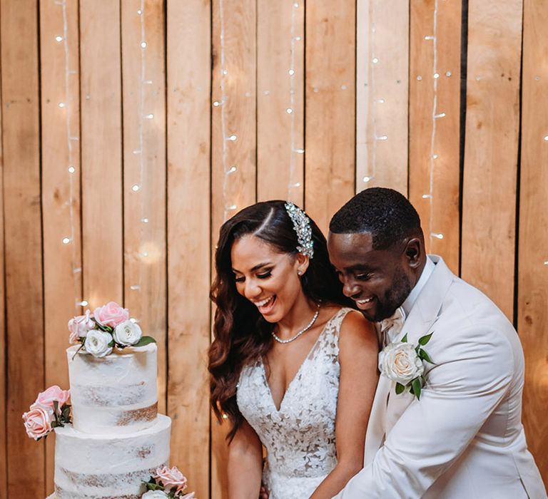 The bride and groom cut their three tier rustic wedding cake decorated with pale pink flowers 