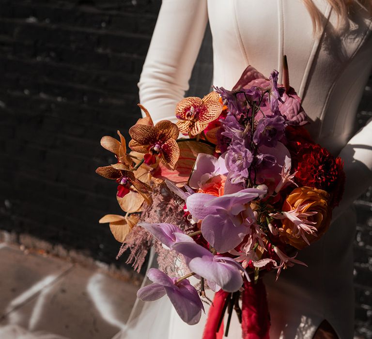 Bride holding orange and purple wedding bouquet with orchids and roses 