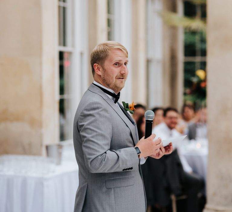 Best man in grey suit and bow tie giving a wedding speech