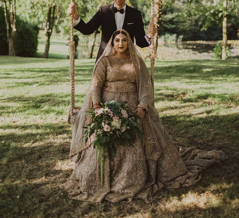 Bride in a gold sari sitting on a swing at Thicket Priory wedding venue in York 